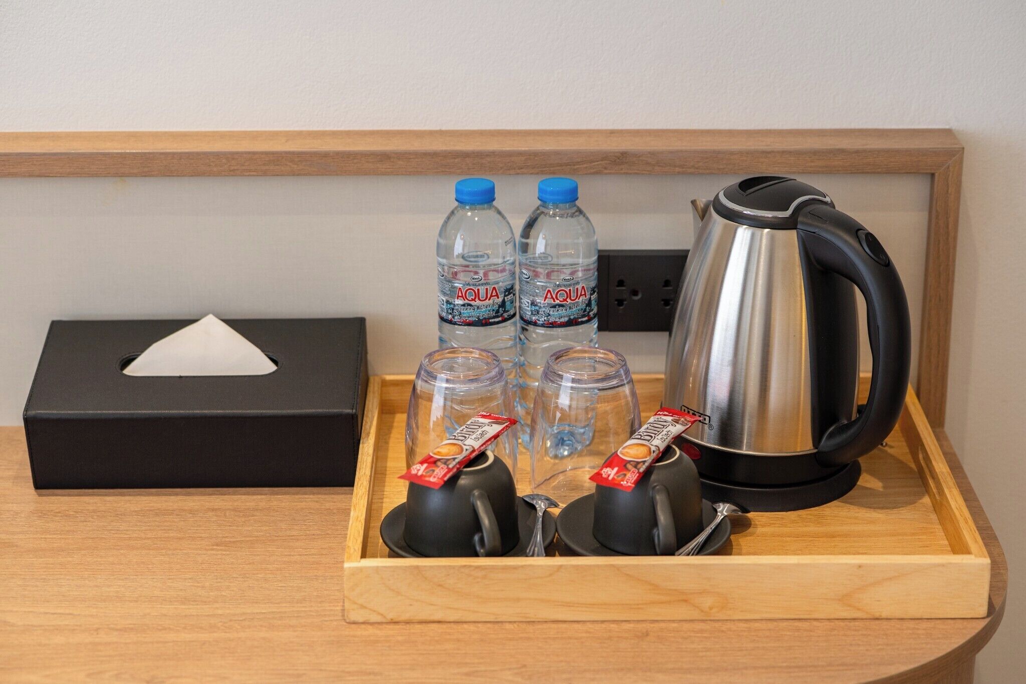 Una bandeja con una caja negra, dos botellas de agua, dos vasos, una tetera y dos tazas con bolsitas de té.