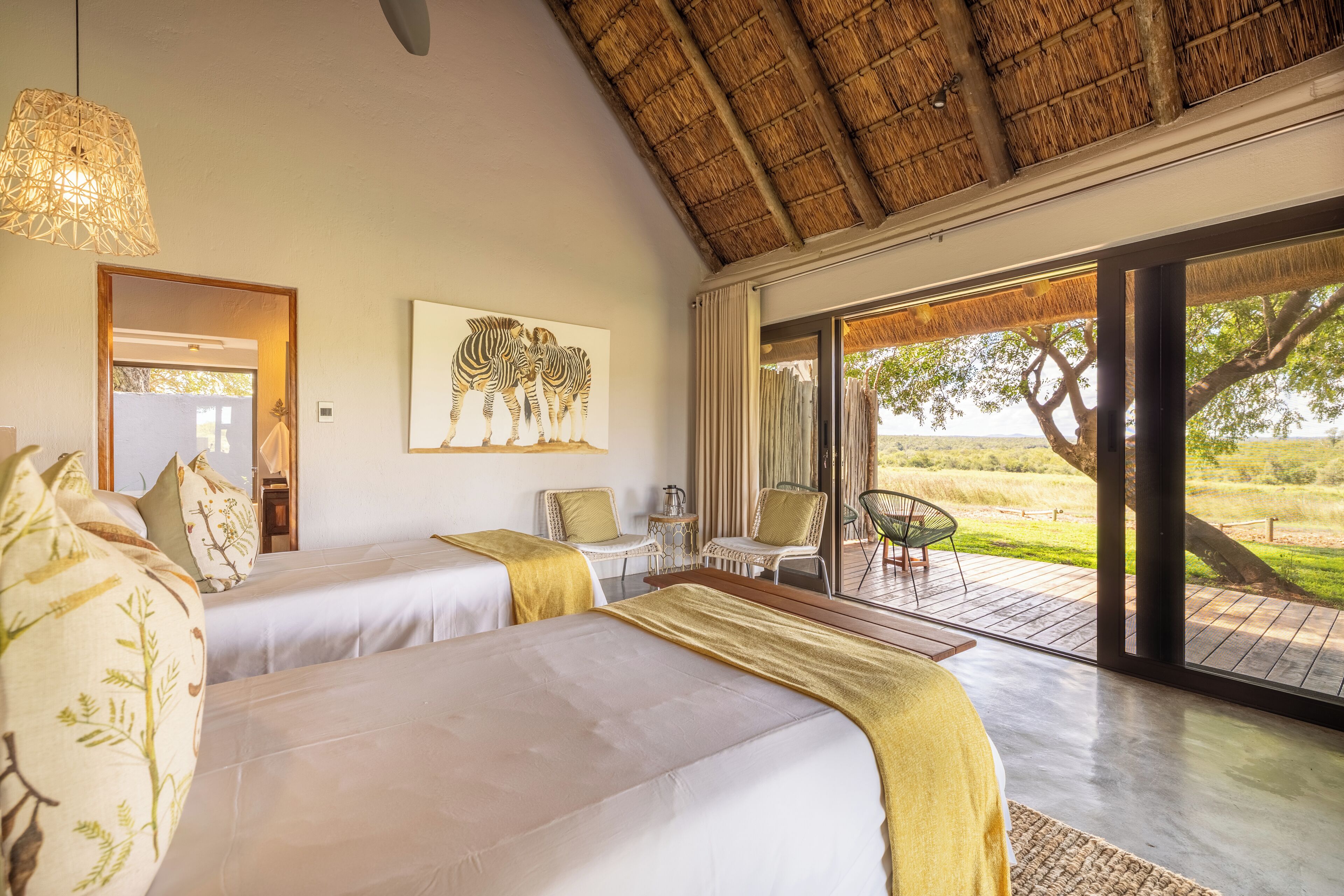 A bedroom with two beds, a large window, a zebra painting, and a view of the outdoors.