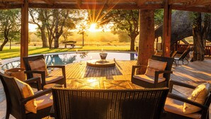 Um deck externo com móveis de vime, uma lareira e vista para uma paisagem natural.