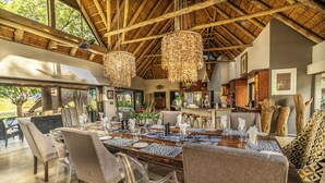 Uma sala de jantar com uma grande mesa de madeira, cadeiras transparentes e lustres de vime pendurados.