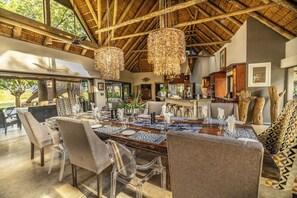 A dining area with a large wooden table, clear chairs, and hanging wicker chandeliers. - Clive's Camp (Hoedspruit)