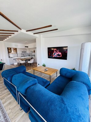 Ein modernes Wohnzimmer mit einem großen blauen Sofa, einem Holztisch und einem flachbildfernseher an der Wand.