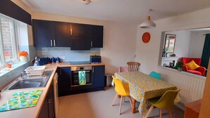 A compact kitchen with dark cabinets, a dining table with yellow chairs, and a red sofa in the living area. - Number One - A colourful family friendly space! (Crossways)