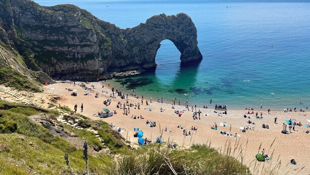 A beach with a natural rock arch formation, clear blue water, and a sandy shore with people. - Number One - A colourful family friendly space! (Crossways)