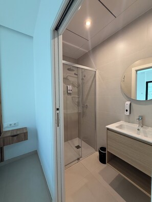 Un baño moderno con ducha acristalada, un lavabo con espejo y un estante de madera.