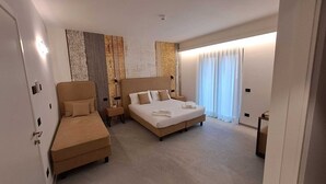A hotel room with a bed, a sofa, a nightstand, and a large window with curtains. - MOUNTAIN SUITE - Hotel Apartment (Tirano)