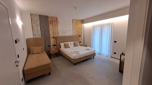 A hotel room with a bed, a sofa, a nightstand, and a large window with curtains.