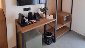 Moderni huone, jossa on taulutelevisio, puinen työpöytä tuolilla, seinälle kiinnitetty hylly ja pieni kasvi.