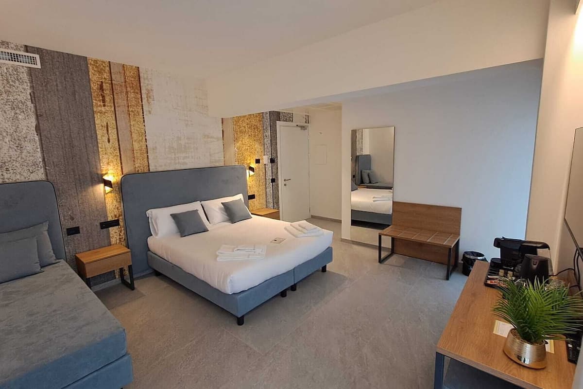 Una habitación de hotel moderna con cama, sofá, escritorio con planta y espejo.