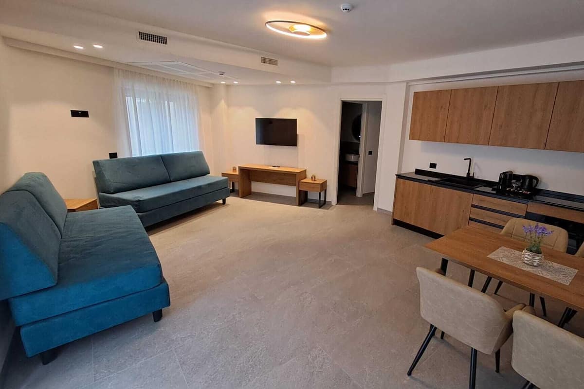 Una sala de estar moderna con un sofá, una mesa de comedor con sillas, una zona de cocina con armarios de madera y un televisor montado en la pared.