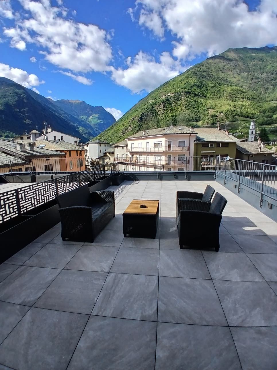 Una terraza en la azotea con mobiliario exterior y vistas a una montaña y edificios.