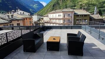 Una terraza en la azotea con mobiliario exterior y vistas a una montaña y edificios.