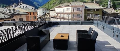 Una terraza en la azotea con mobiliario exterior y vistas a una montaña y edificios.