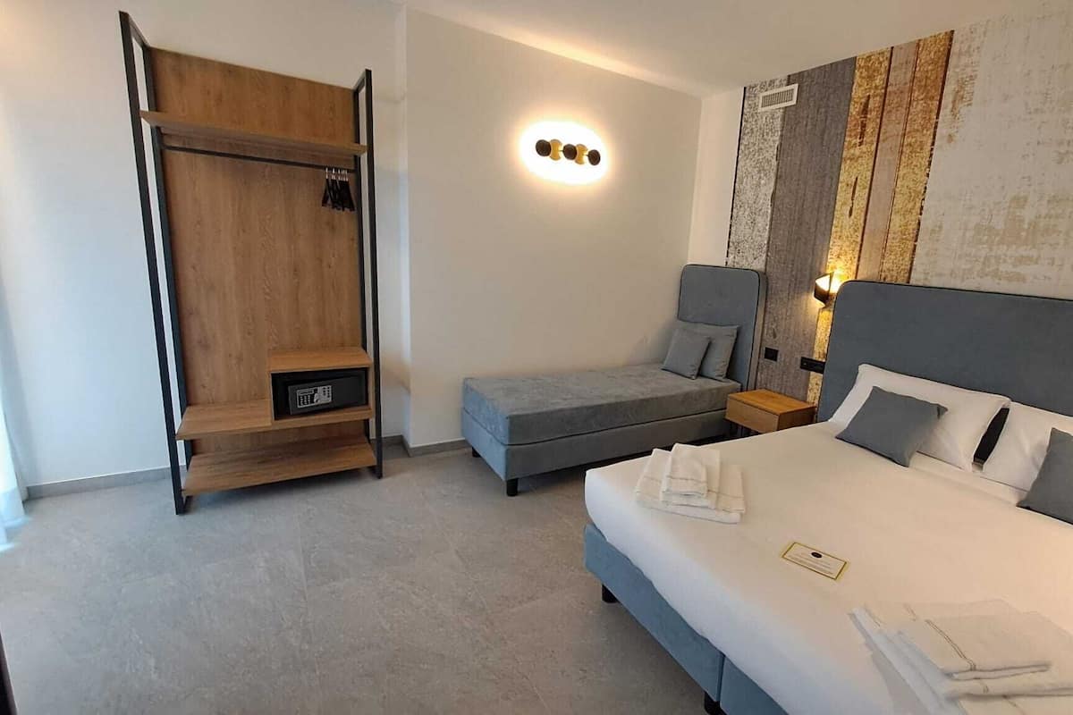 Una habitación de hotel con una cama grande, una cama más pequeña, un armario, una lámpara de pared y un panel decorativo.