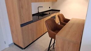 A modern kitchen with wooden cabinets, a black countertop, and a bar area with stools. - MOUNTAIN SUITE - Hotel Apartment (Tirano)