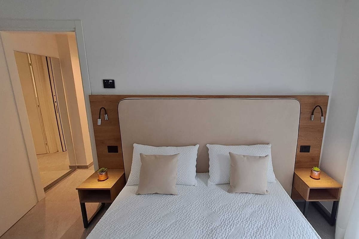 Habitación de hotel con cama, dos mesitas de noche, un buró, una puerta y un aplique de pared.