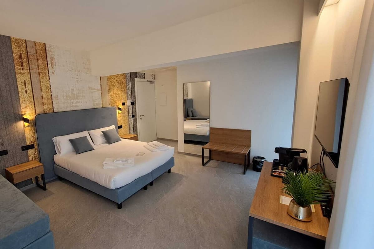 Habitación de hotel moderna con una cama grande, un escritorio con una planta, un televisor y un espejo.
