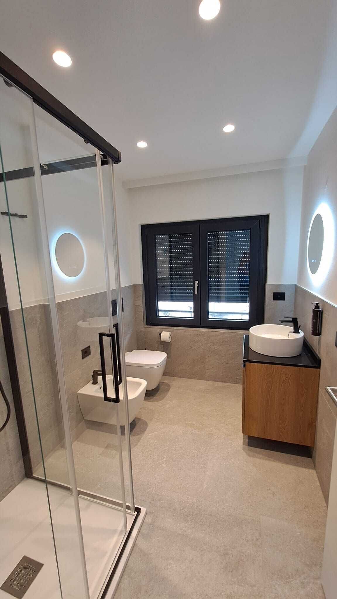 Een moderne badkamer met een douchecabine van glas, twee toiletten, een wastafel en een meubel met een spiegel.