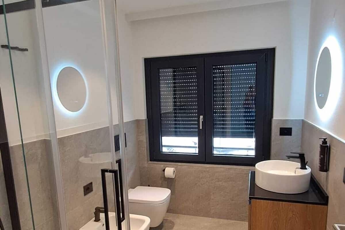Un baño moderno con cabina de ducha de vidrio, dos inodoros, un lavabo y un mueble de tocador con espejo.