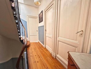 Un estrecho pasillo con suelo de madera, puertas blancas y una escalera a la izquierda.