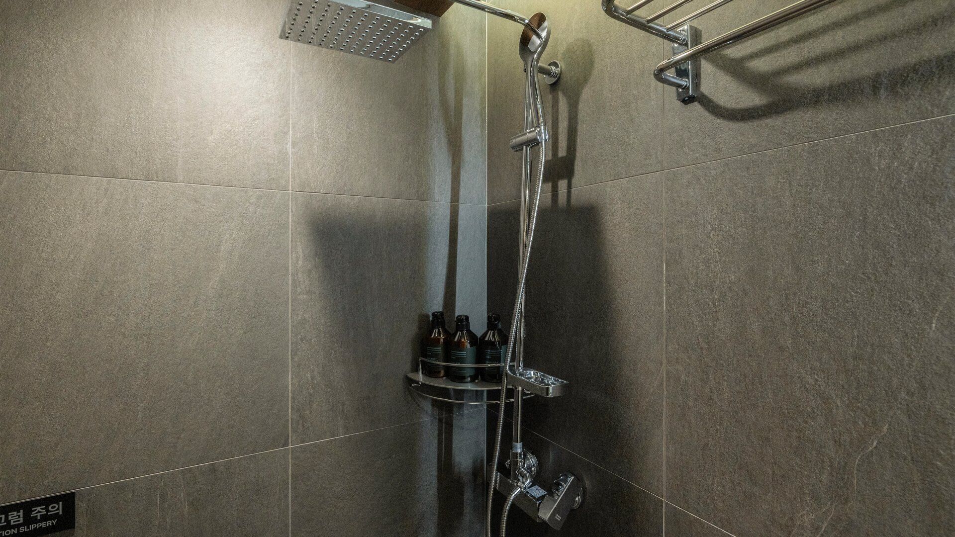A shower area with a handheld showerhead, a wall-mounted hand dryer, and a towel rack.