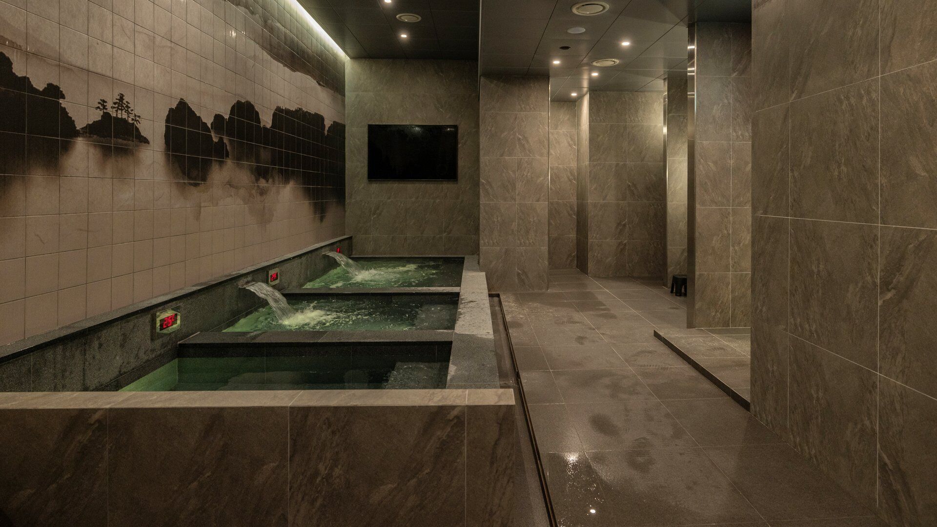 A spa area with three hot tubs, tiled walls, and a digital clock.