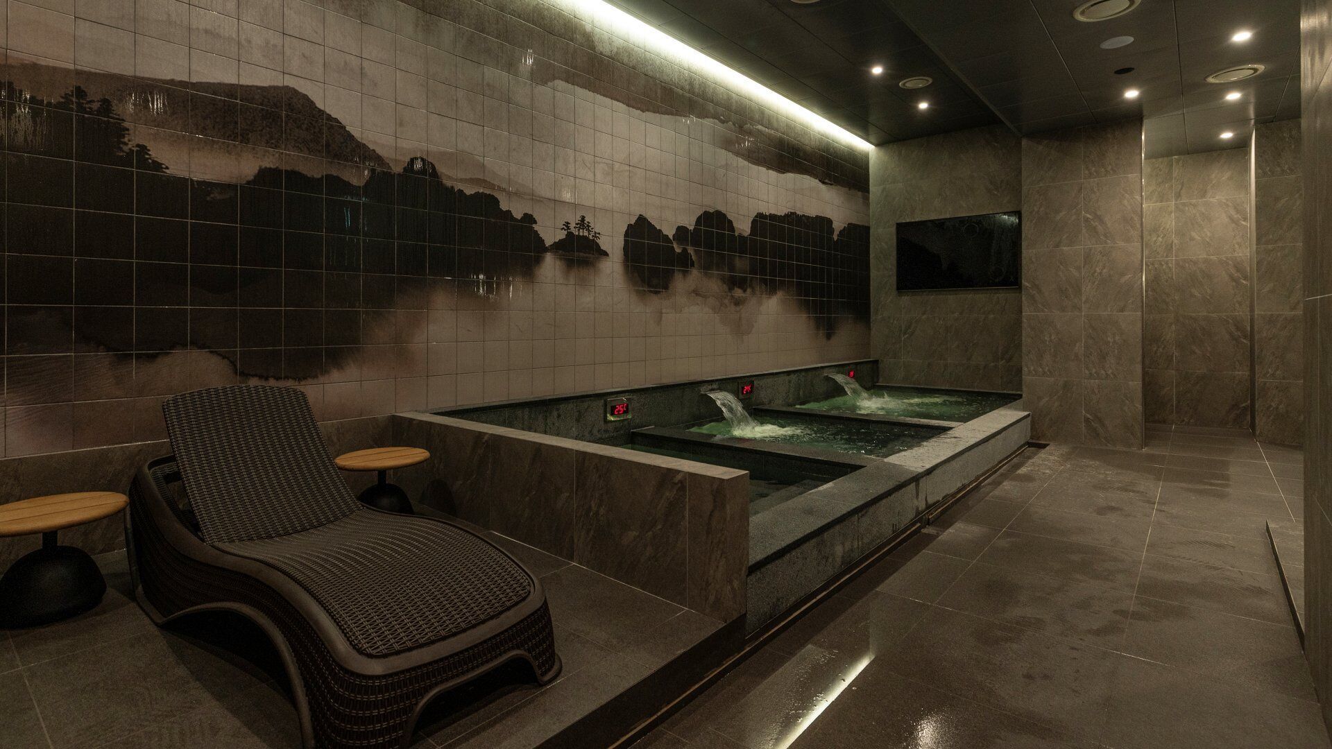 Un área de spa con una bañera de hidromasaje, una silla de descanso y una pared decorada con un paisaje montañoso.