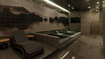Un área de spa con una bañera de hidromasaje, una silla de descanso y una pared decorada con un paisaje montañoso.