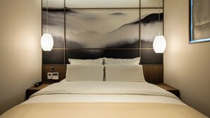 Hotellihuone, jossa on sänky, kaksi yöpöytää, yövalaisin, seinälle asennettu ohjauspaneeli ja kaksi riippuvalaisinta.