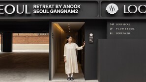 A woman entering a modern building with a sign indicating 'RETREAT BY ANOOK SEOUL GANGNAM2'. - Loop Seoul Hotel Retreat by Anook Seoul Gangnam 2 (Seoul)