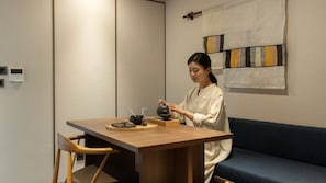 A person seated at a wooden table with a teapot, cups, and a tray. There is a blue sofa and a wall with a geometric pattern. - Loop Seoul Hotel Retreat by Anook Seoul Gangnam 2 (Seoul)