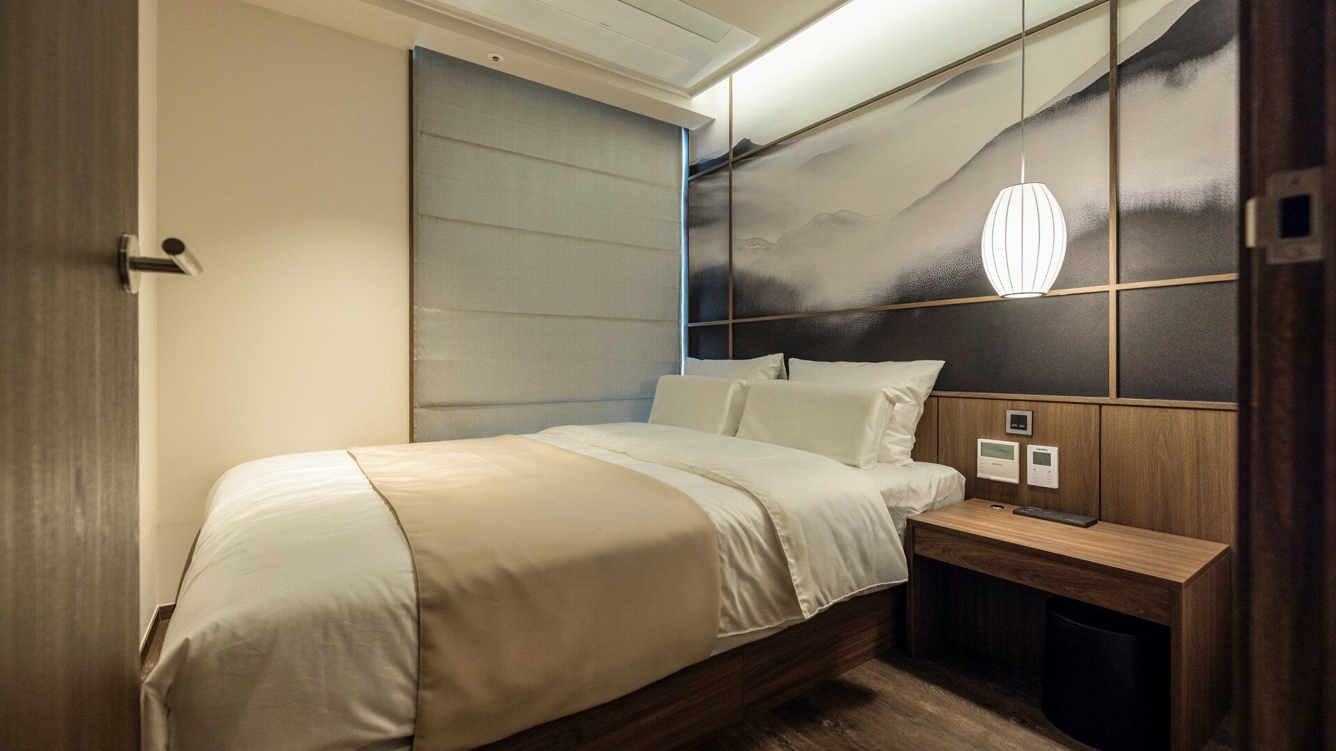 Une chambre d’hôtel moderne équipée d’un lit, d’une table de chevet et d’un luminaire fixé au mur.