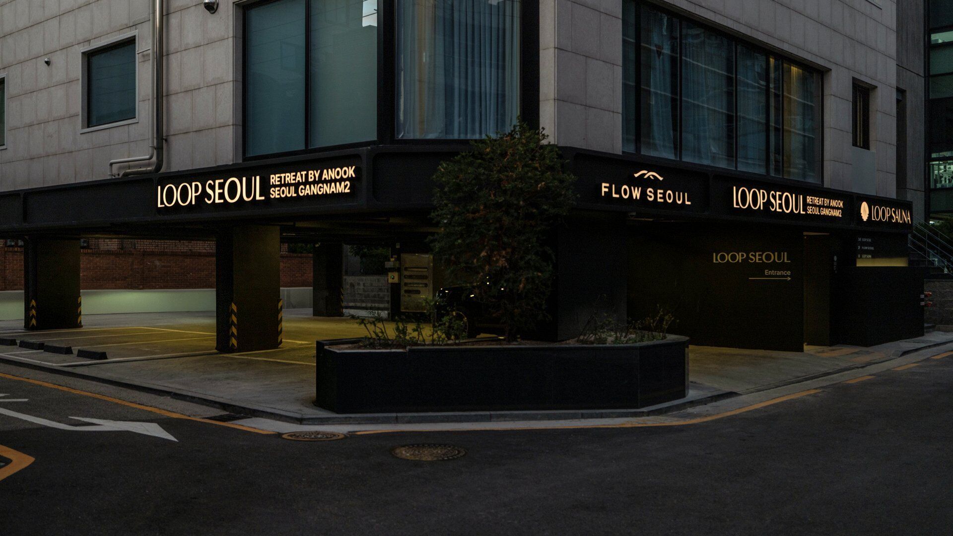 A building with 'LOOP SEOUL' signage, a parking area, and a small landscaped area with plants.