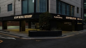 Rakennuksessa on kyltti, jossa lukee ”LOOP SEOUL”, parkkialue ja pieni, kasveilla koristeltu alue.
