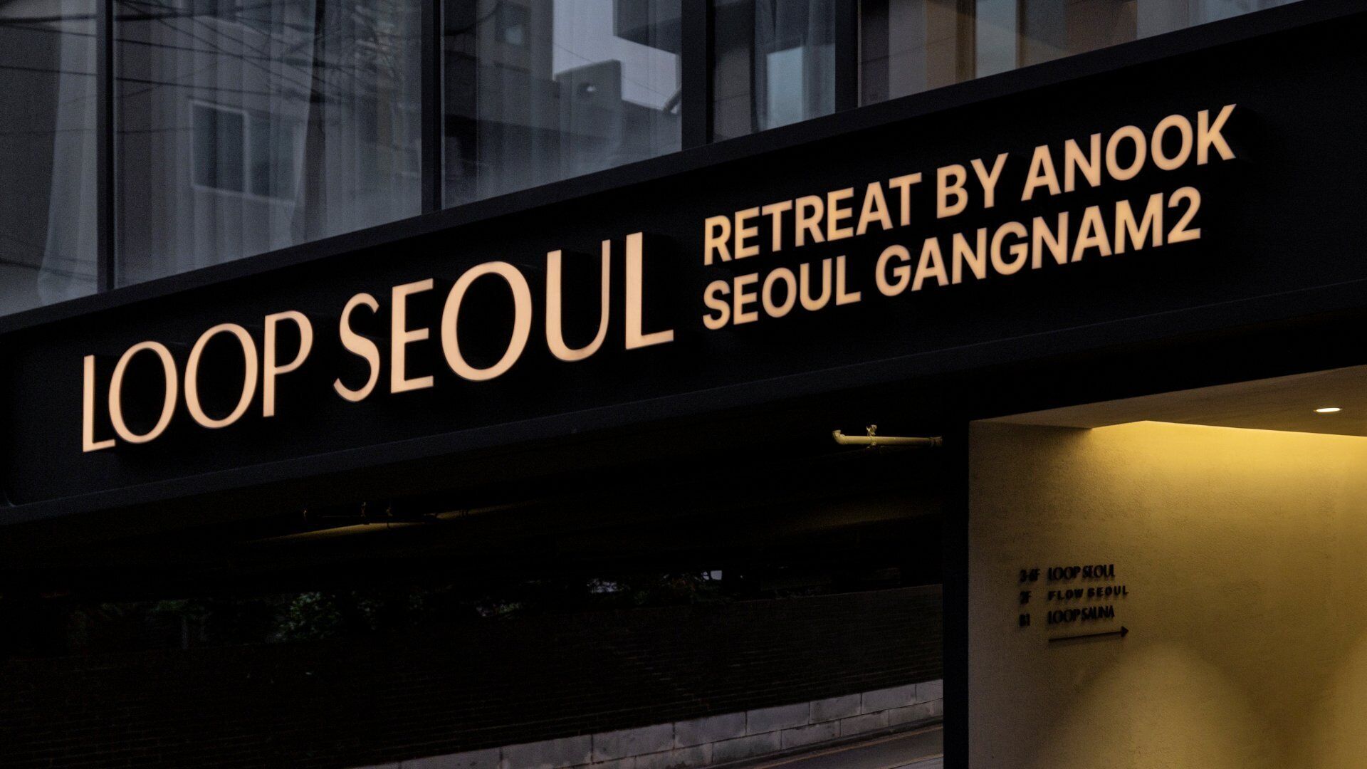 Une enseigne indiquant « LOOP SEOUL RETREAT BY ANOOK SEOUL GANGNAM2 », avec des flèches directionnelles et une vue partielle de la façade d’un bâtiment.
