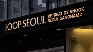 Une enseigne indiquant « LOOP SEOUL RETREAT BY ANOOK SEOUL GANGNAM2 », avec des flèches directionnelles et une vue partielle de la façade d’un bâtiment.