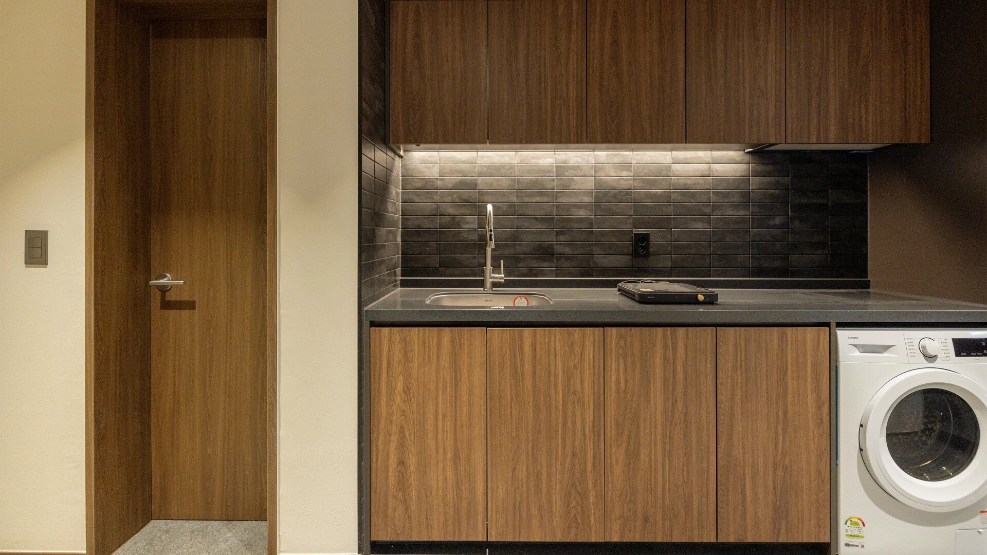 A compact kitchen with a built-in washing machine, a sink, and wooden cabinetry.