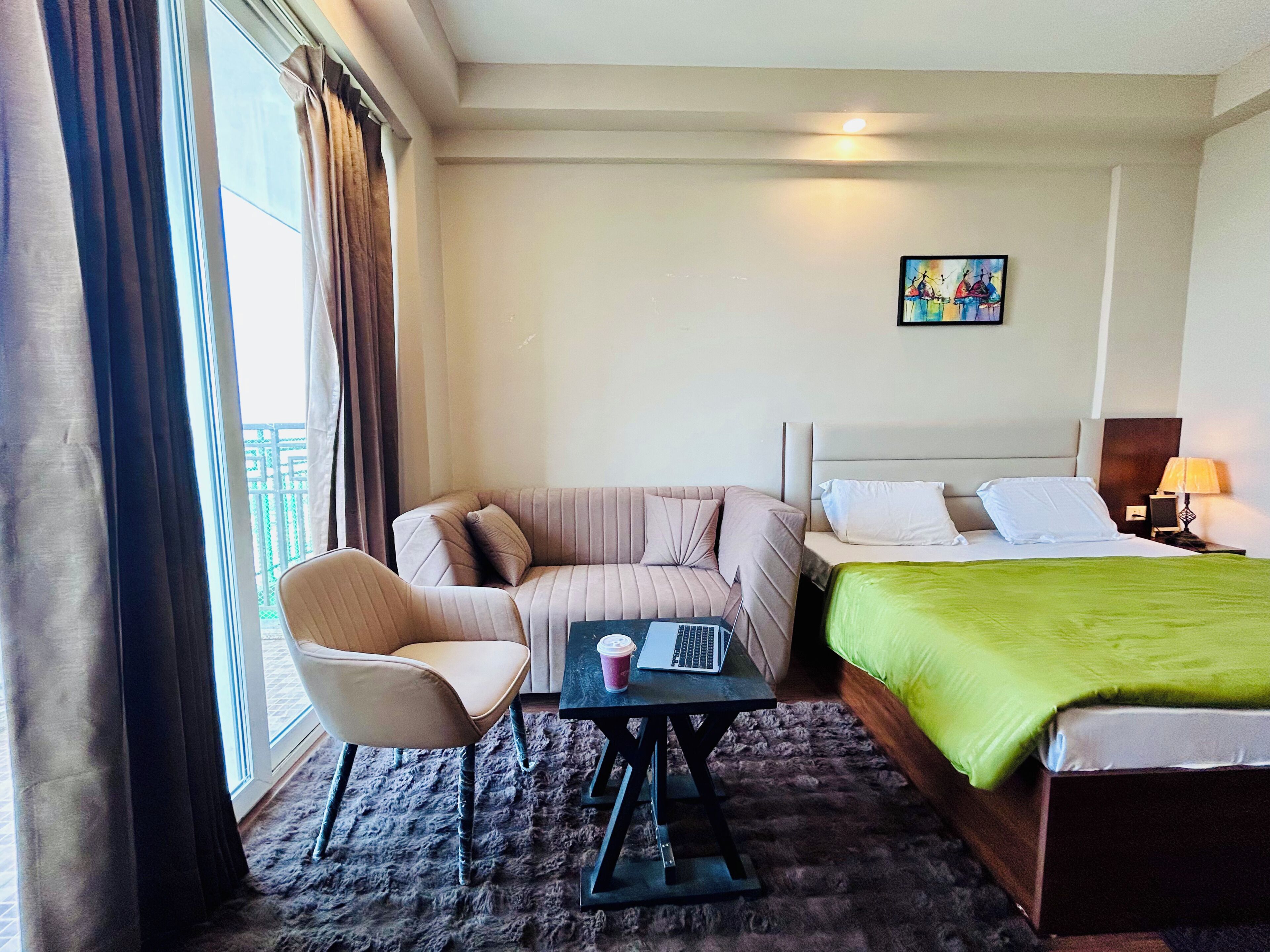 Une chambre d’hôtel avec un lit, un canapé, une chaise, une petite table et une fenêtre avec des rideaux.
