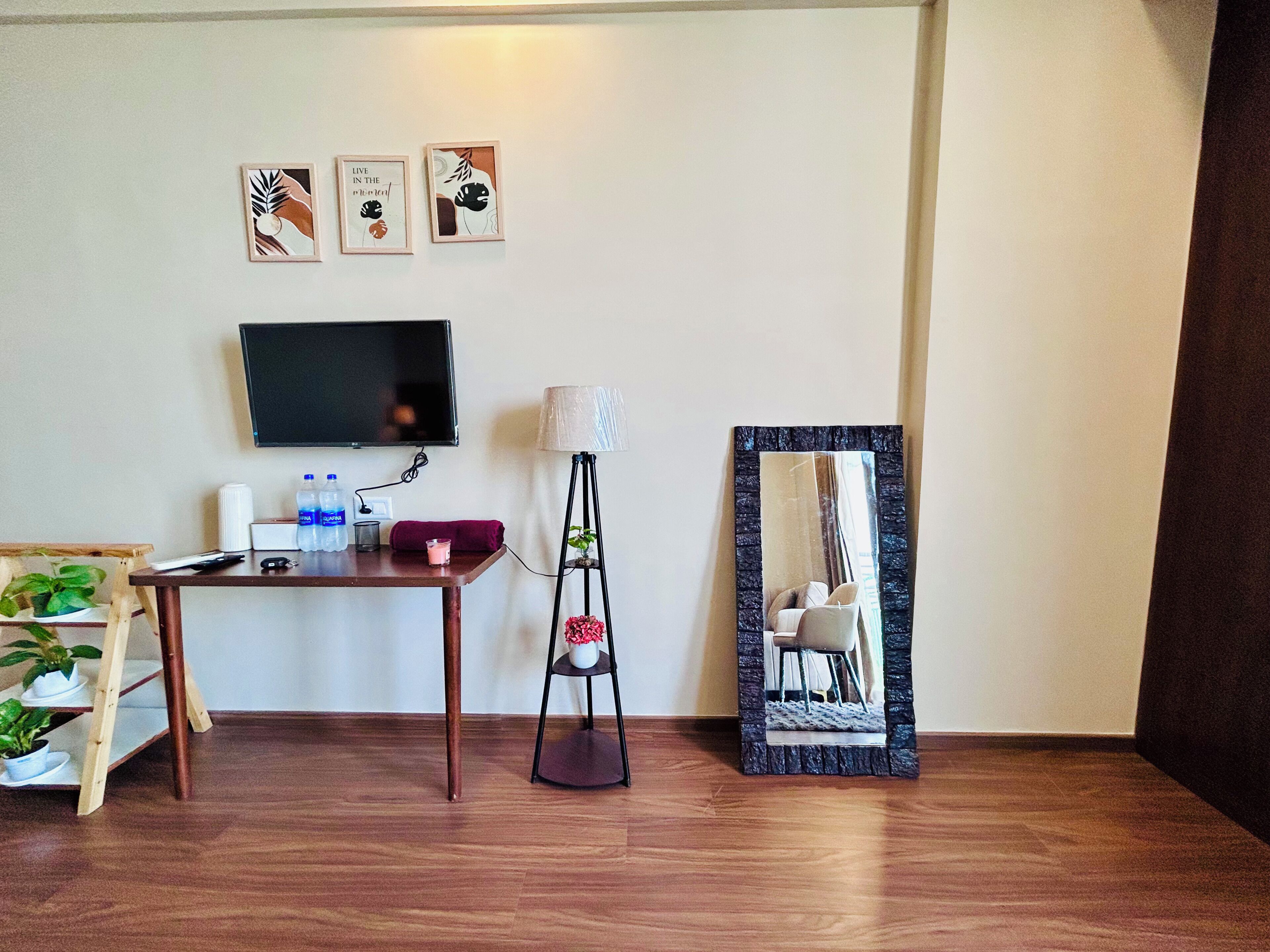 Quarto com piso de madeira, uma escrivaninha, televisão de tela plana, abajur, espelho e obras de arte na parede.