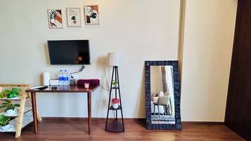 Quarto com piso de madeira, uma escrivaninha, televisão de tela plana, abajur, espelho e obras de arte na parede.