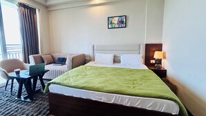 Une chambre d’hôtel avec un lit, un bureau avec un ordinateur portable, une chaise, une table de chevet avec une lampe et un tableau au mur.