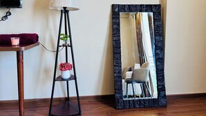 Une pièce comprenant un lampadaire, un miroir avec un cadre en pierre, une petite table avec une bougie et une chaise.