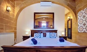 A hotel room with a large bed, a mirror above the bed, stone walls, and a radiator. - Stunning 6-Bed Gozo Villa, Private Pool & Tropical Oasis (Gozo)