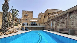 Una piscina con un muro in pietra su un lato e un edificio con finestre ad arco e una torre.