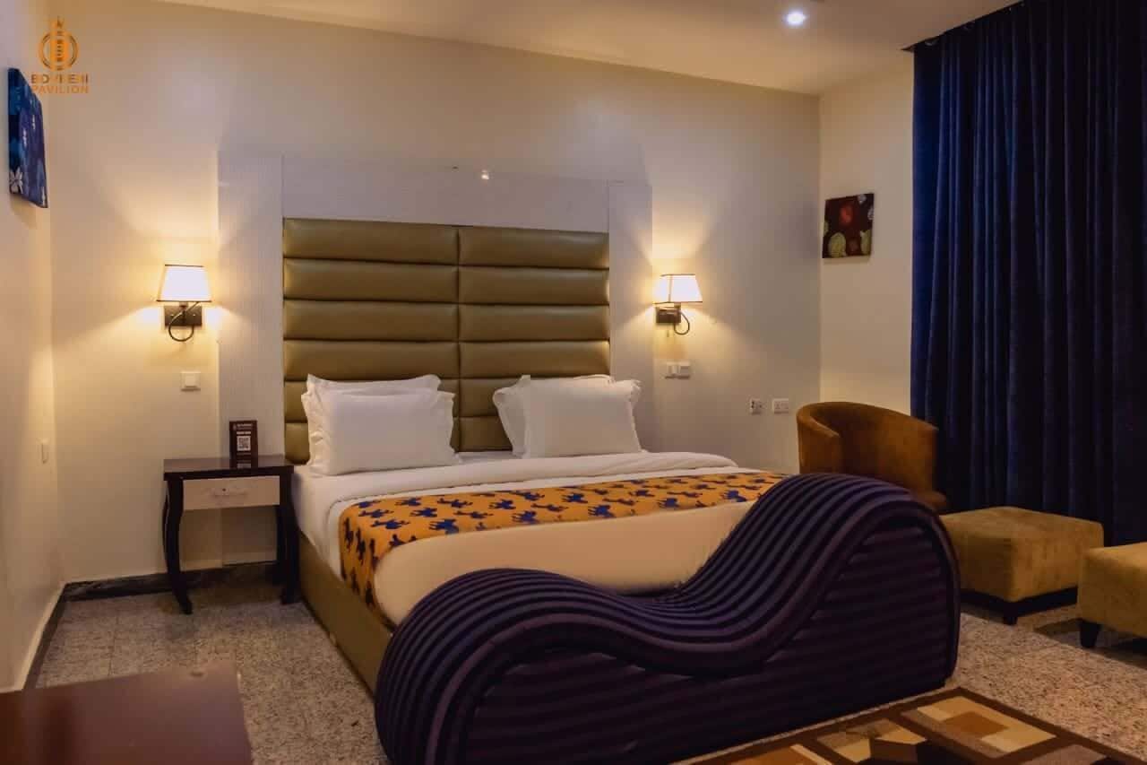 A hotel room with a bed, two bedside lamps, a chair, a small table, and a curtain.