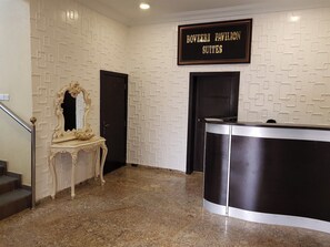 Un espace d’accueil doté d’un sol en marbre, d’un comptoir de réception, d’un miroir à cadre orné et d’une enseigne au-dessus du comptoir indiquant « BOVEERI PAVILION SUITES ».