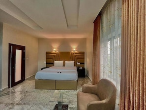 Habitación de hotel con cama, mesitas de noche, una silla y vistas al exterior.