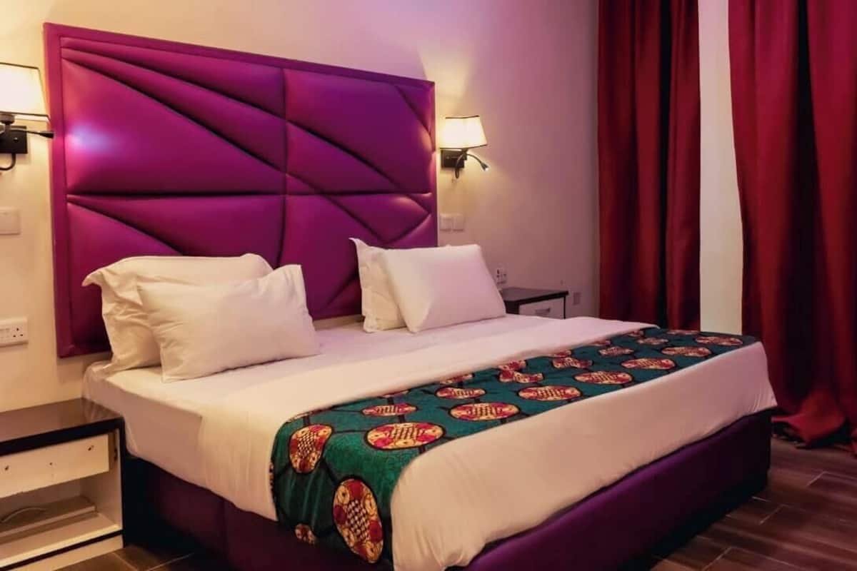 Une chambre dâhĂŽtel avec un grand lit, une tĂȘte de lit, deux lampes de chevet, une table de chevet et une fenĂȘtre avec des rideaux rouges.