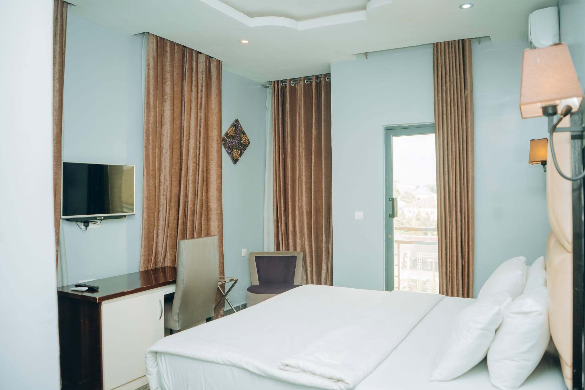 A hotel room with a bed, a desk, a chair, a TV, and curtains.