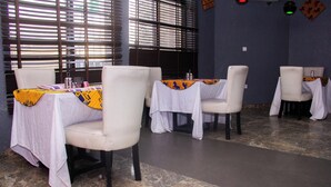 Un interior de restaurante con mesas cubiertas de manteles blancos, sillas y una pared decorativa.